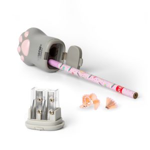 A grey pencil sharpener shaped like a cat's paw. A pink pencil with a colourful pattern is being sharpened inside it, and the shavings are scattered on a white surface next to a separate double pencil sharpener with a clear plastic top. The cat paw sharpener has a door on the side that is open, revealing the sharpening blade and the shavings inside.
