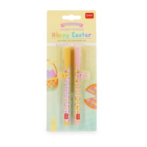 Retail packaging for the Limited Edition Legami Lovely Friends Hoppy Easter gel pen set against an Easter picnic card illustrated with an egg basket and pie. The pack contains two 0.5 mm gel pens: a yellow and pink pen with a chick accessory and metallic purple ink, and a pastel pink and yellow pen with a bunny accessory and metallic pink ink.